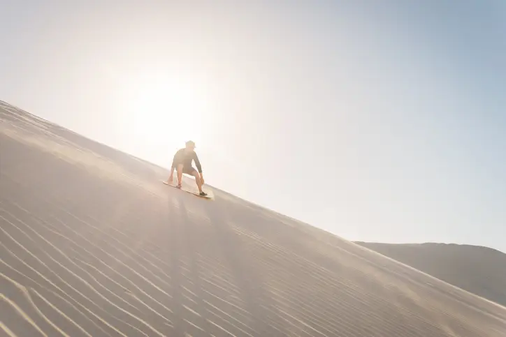 Guy sandboarding down a dune.