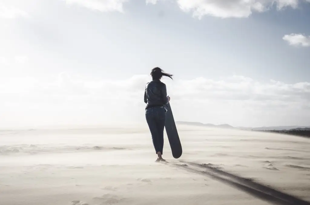 Woman walking with sandboard on a dune.